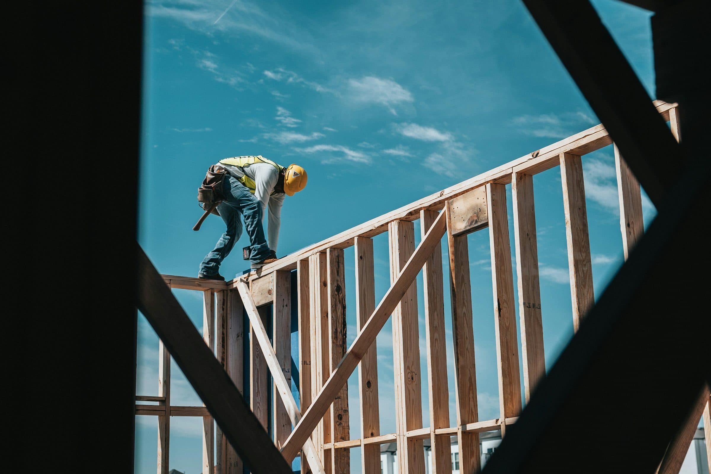 A framer standing on top of a new wall frame against a blue sky