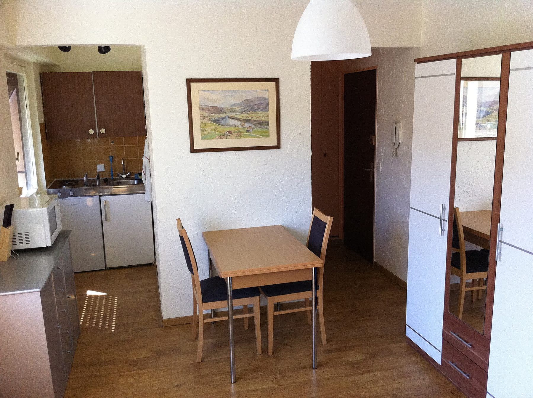 A furnished studio with a small table, two chairs and a kitchenette